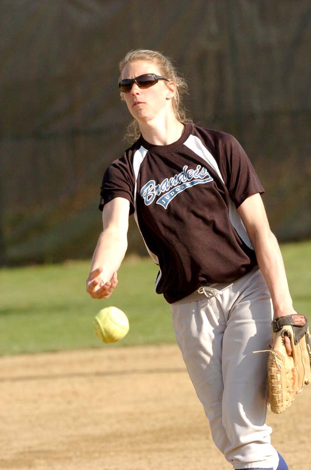 A softball player, wearing sunglasses, throwing a pitch during a game